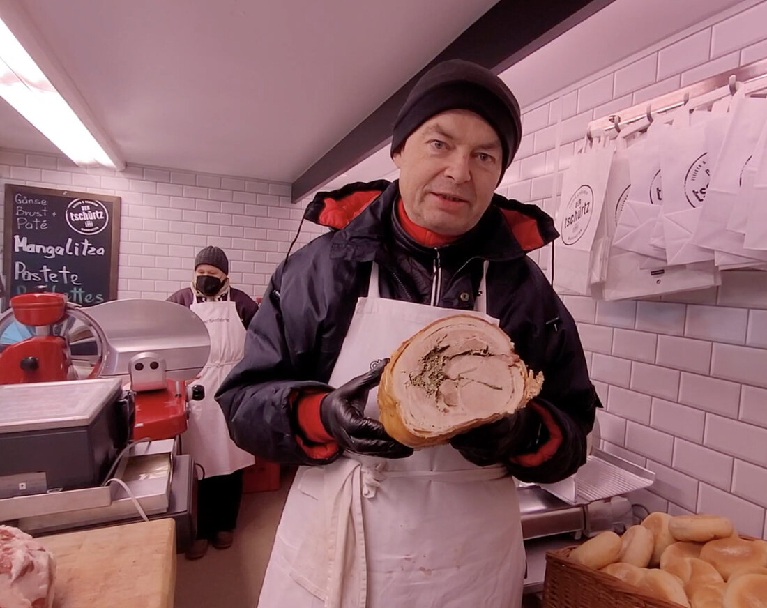 Wir haben hier einen besonderen Schweinsbraten, den haben wir den Italienern abgeschaut,  Porchetta romana, den römischen Schweinsbraten. Ursprünglich werden ganze Schweine gerollt, ich habe ein Karree genommen und das Bauchfleisch mit Schwarte, ausgelöst und wird es innen mit frischen Kräutern, Knoblauch, Meersalz und Pfefferinnen gewürzt, dann wird es zusammengeschnürt und gebraten. So lange bis die Schwarte knusprig ist. Das richte ich zum Beispiel für Grillfeste her, das kann man bestellen, das hat dann drei, vier, fünf, sechs, sieben, acht Kilo. Das steckt man dann auf einen Spieß und grillt das idealerweise auf dem Holzkohlengrill. Man kann das mit Freunden beobachten, …