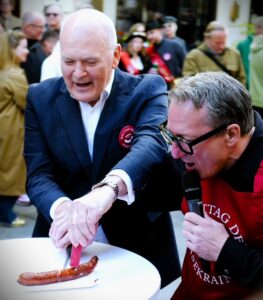 Die Grillsaison wurde „angeschnitten“. Dr. Franz Radatz mit seinem Cousin Robert Palfrader und der Eröffnungswurst. © Roland Graf
